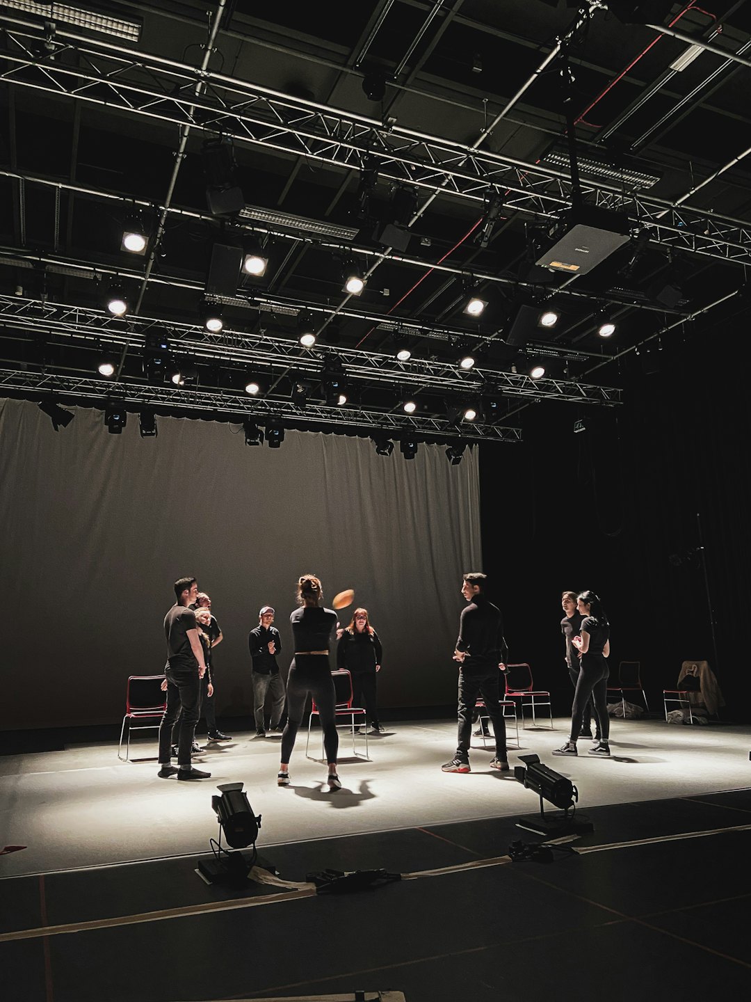 Young adults rehearse on a dimly lit stage with spotlights.