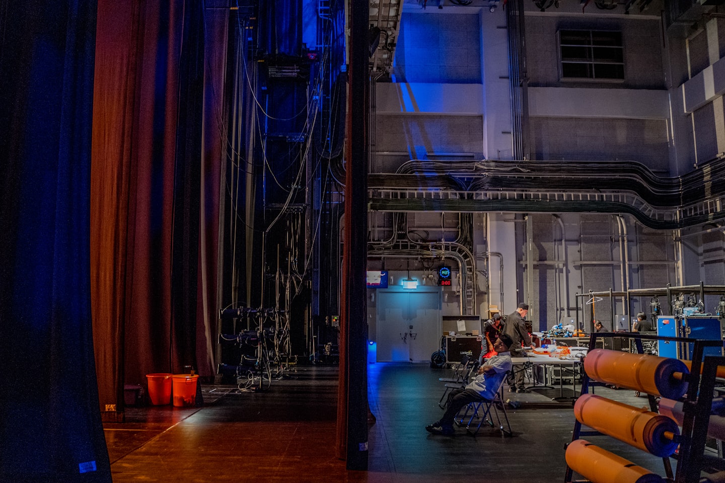 Stage crew members work among technical equipment and rigging backstage.