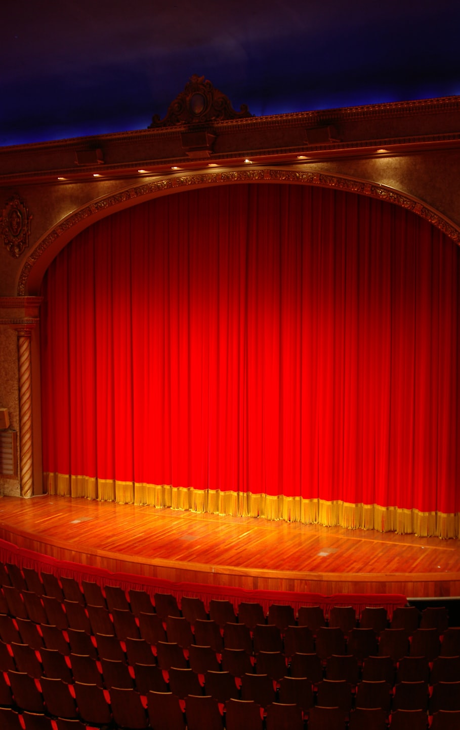 Empty theater stage with a red velvet curtain and wooden floor.