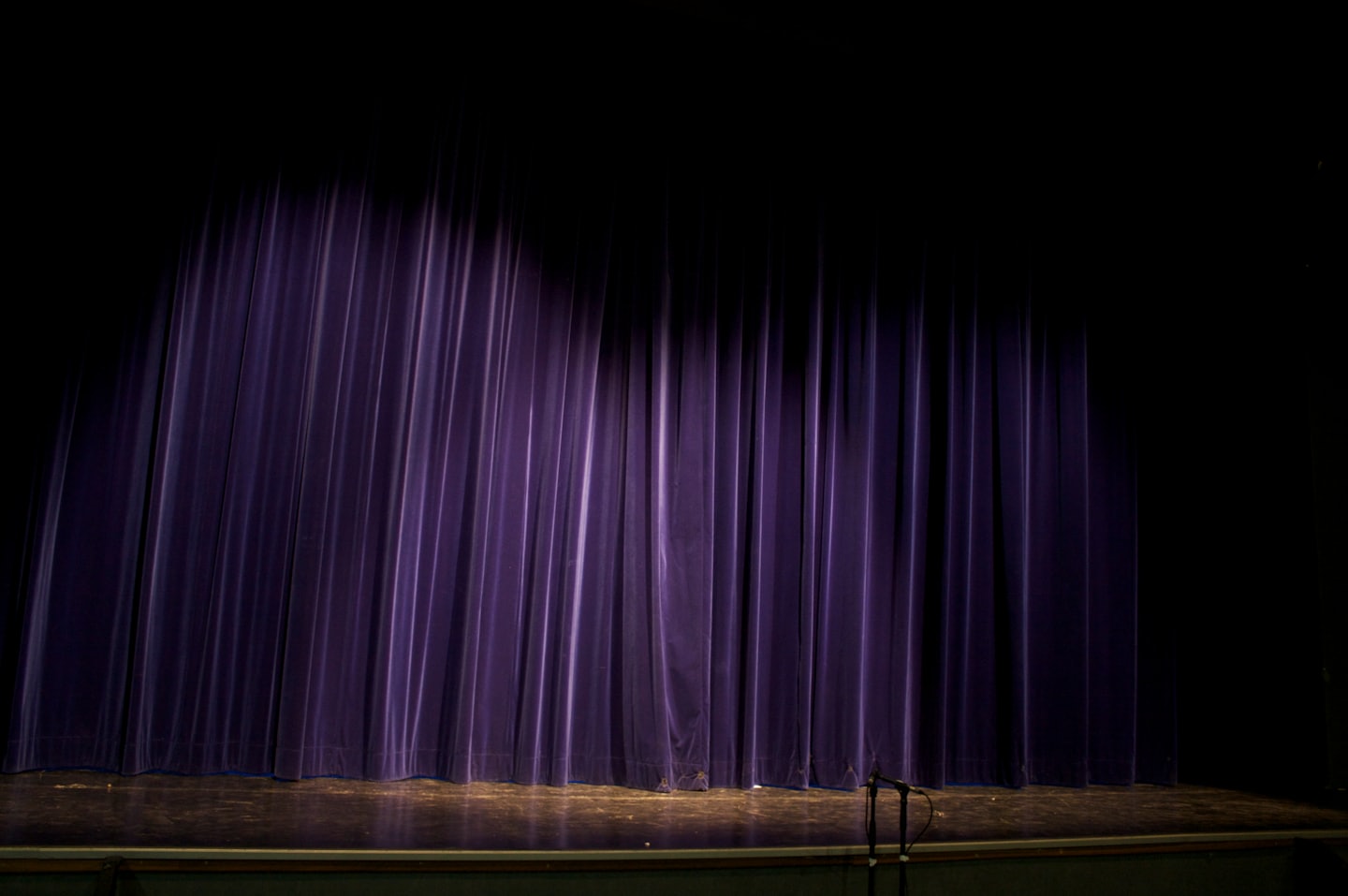 Spotlight on purple stage curtains in an empty theater.