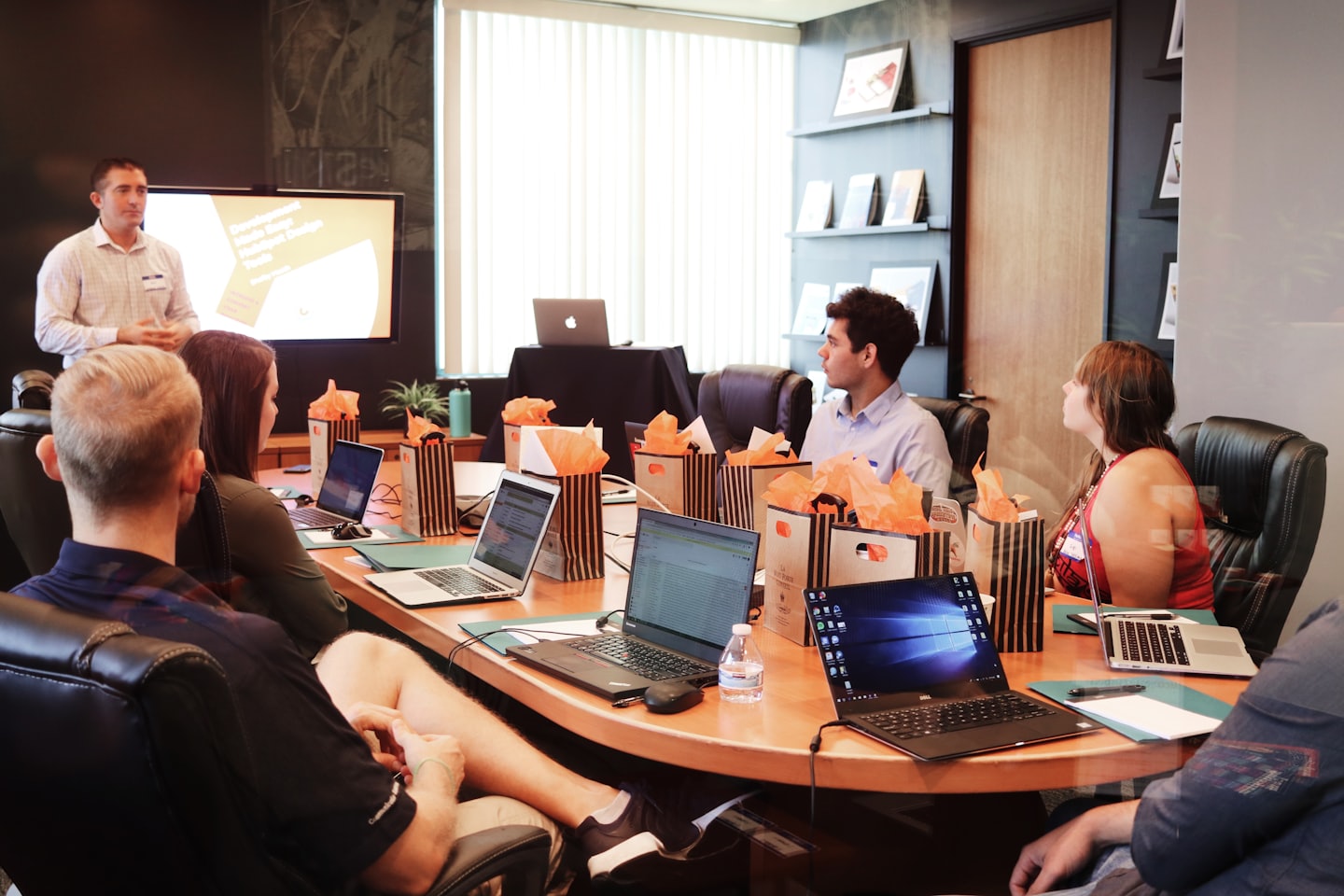 Professionals at a conference table with laptops and gift bags.
